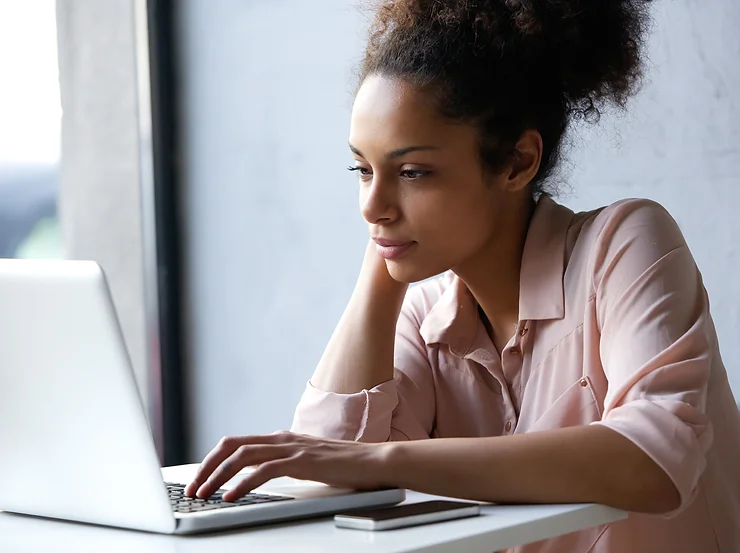 Woman in a pink shirt using a laptop at a desk.