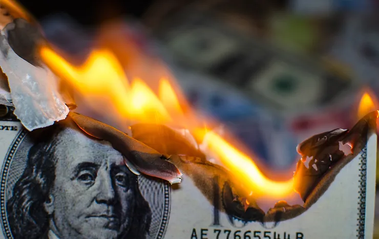 Close-up of a burning US hundred-dollar bill with visible flames and partially charred edges.