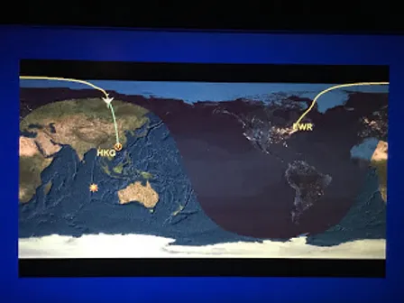 Map showing a flight path from Hong Kong (HKG) to Newark (EWR) with a yellow line across Asia and the Pacific, overlaid on a world map with nighttime shading.