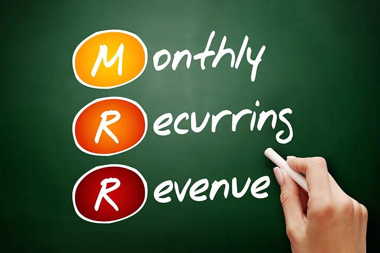 Hand writing "MRR" on a green chalkboard, with each letter representing "Monthly Recurring Revenue" in orange and red circles.