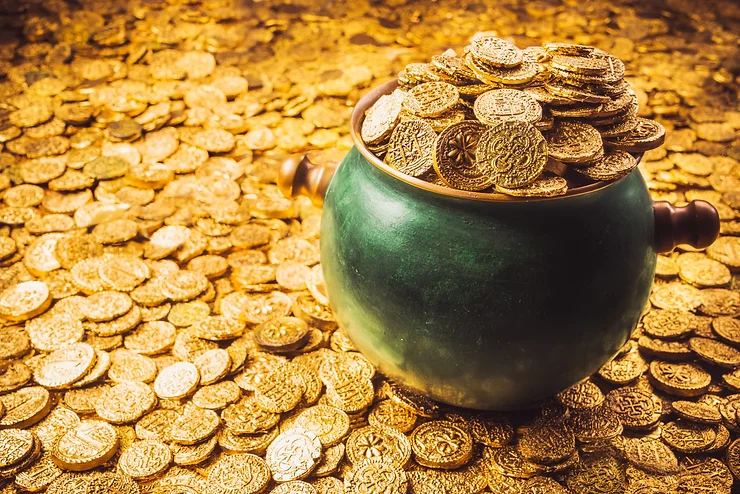 A green pot overflows with gold coins, surrounded by more coins scattered on the ground.