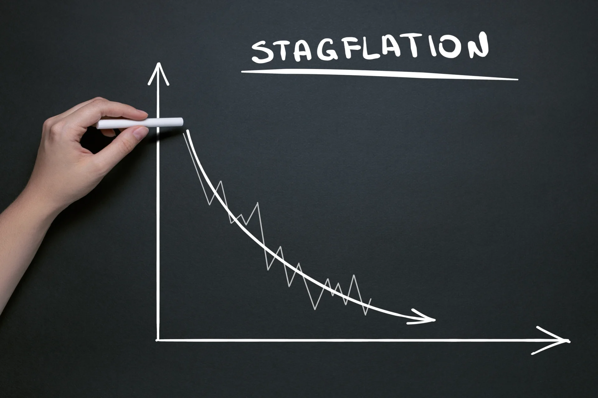 Hand drawing a downward sloping graph on a chalkboard labeled "Stagflation," indicating economic stagnation with inflation.