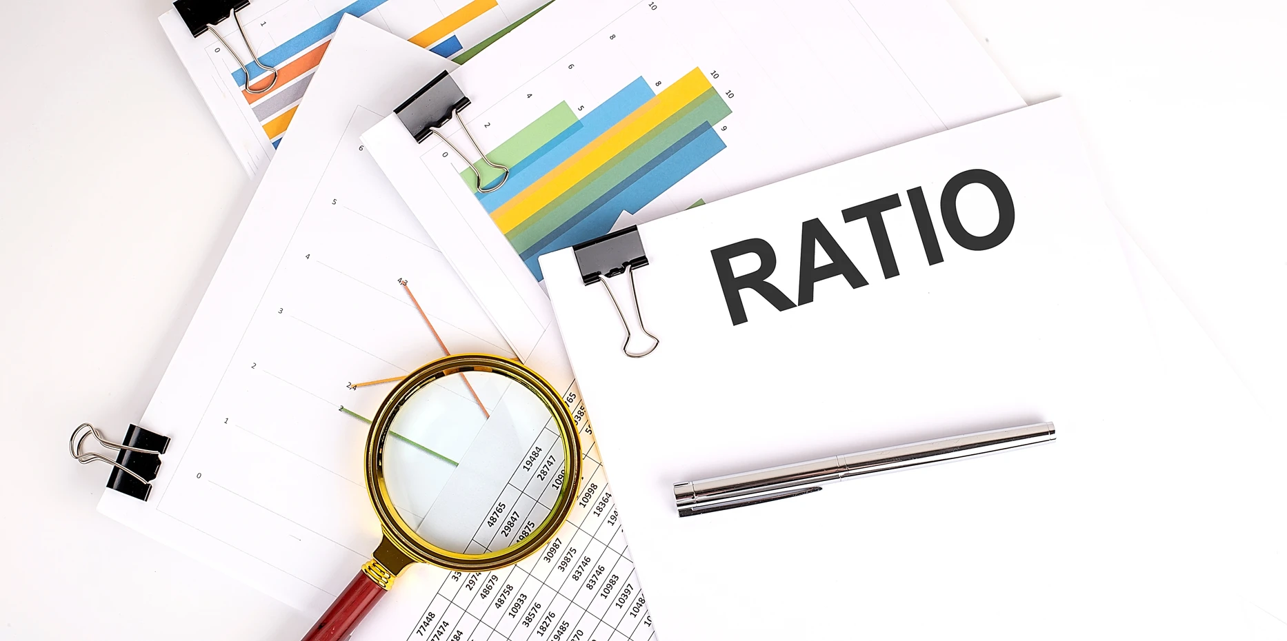 Magnifying glass on spreadsheets with colorful graphs and documents labeled "RATIO.
