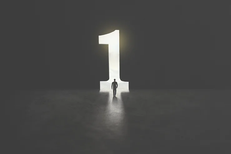 A lone person walks into a large, illuminated number one, set against a dark background.