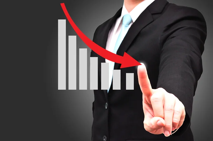 Person in a suit pointing at a downward trend graph with a red arrow on a dark background.