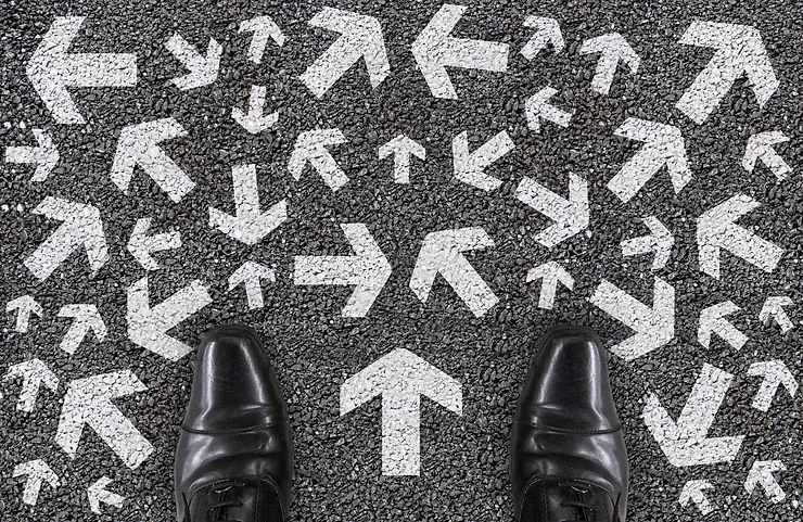 Black shoes facing a road with many white arrows pointing in different directions, suggesting confusion or multiple choices.