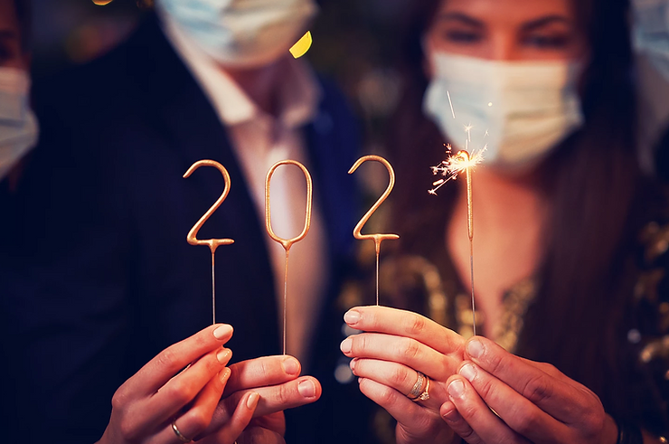 Three people wearing masks hold sparkler candles shaped as "2021," with one candle lit.