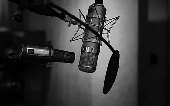 Two professional microphones with a pop filter in a recording studio setting. Black and white image.
