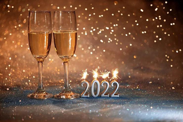 Two champagne glasses beside a lit "2022" sparkler decoration on a glittery background.