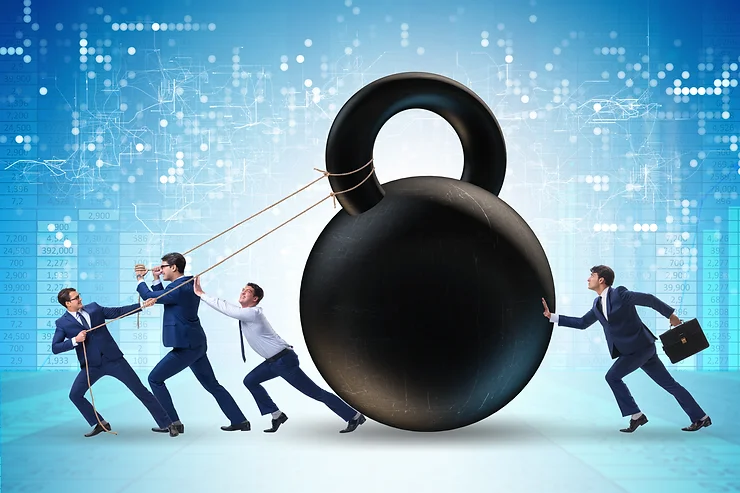 A group of businesspeople in suits attempting to lift a large kettlebell using ropes, with one person pushing it from behind. Background features digital and financial graphics.