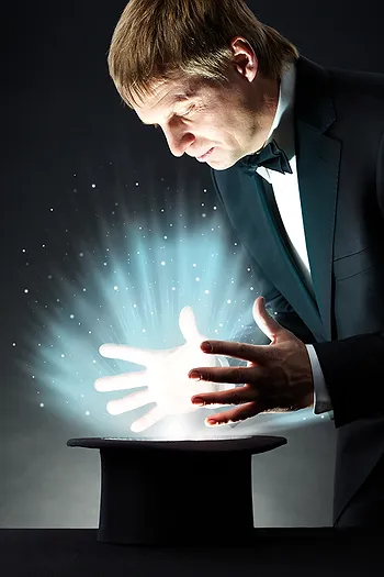 A magician in a tuxedo, with glowing hands, performs a trick over a top hat emitting light and sparkles.