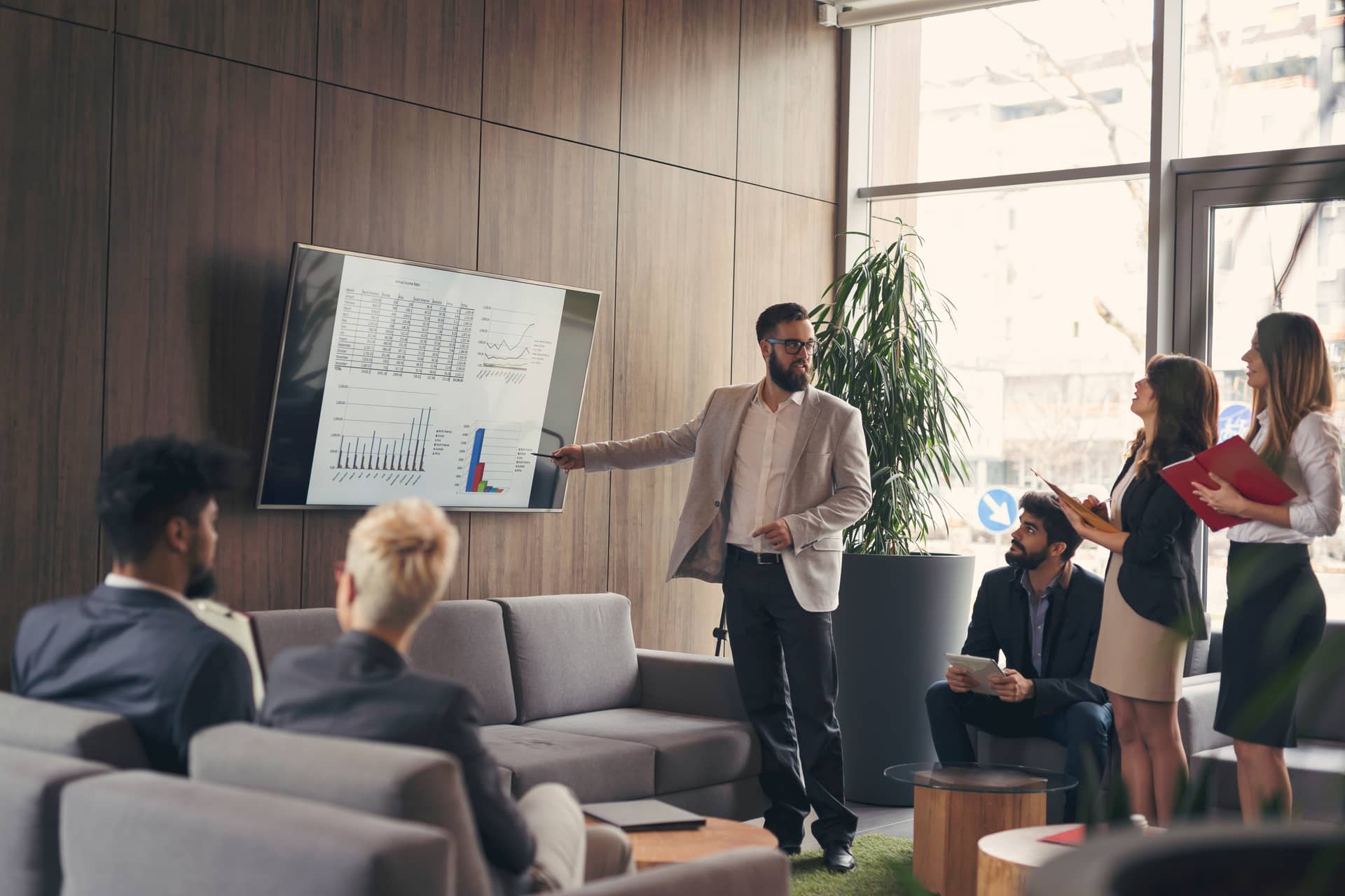 A man presents charts on a screen to four colleagues in a modern office setting.