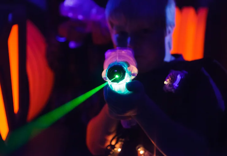 Person aiming a glowing laser tag gun in a dark, neon-lit environment.