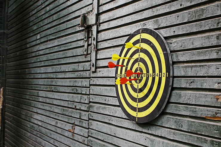 A dartboard with yellow and red darts is mounted on a weathered wooden wall.