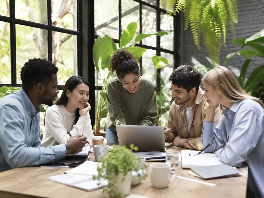 Diverse employees collaborating around a laptop in a bright workspace